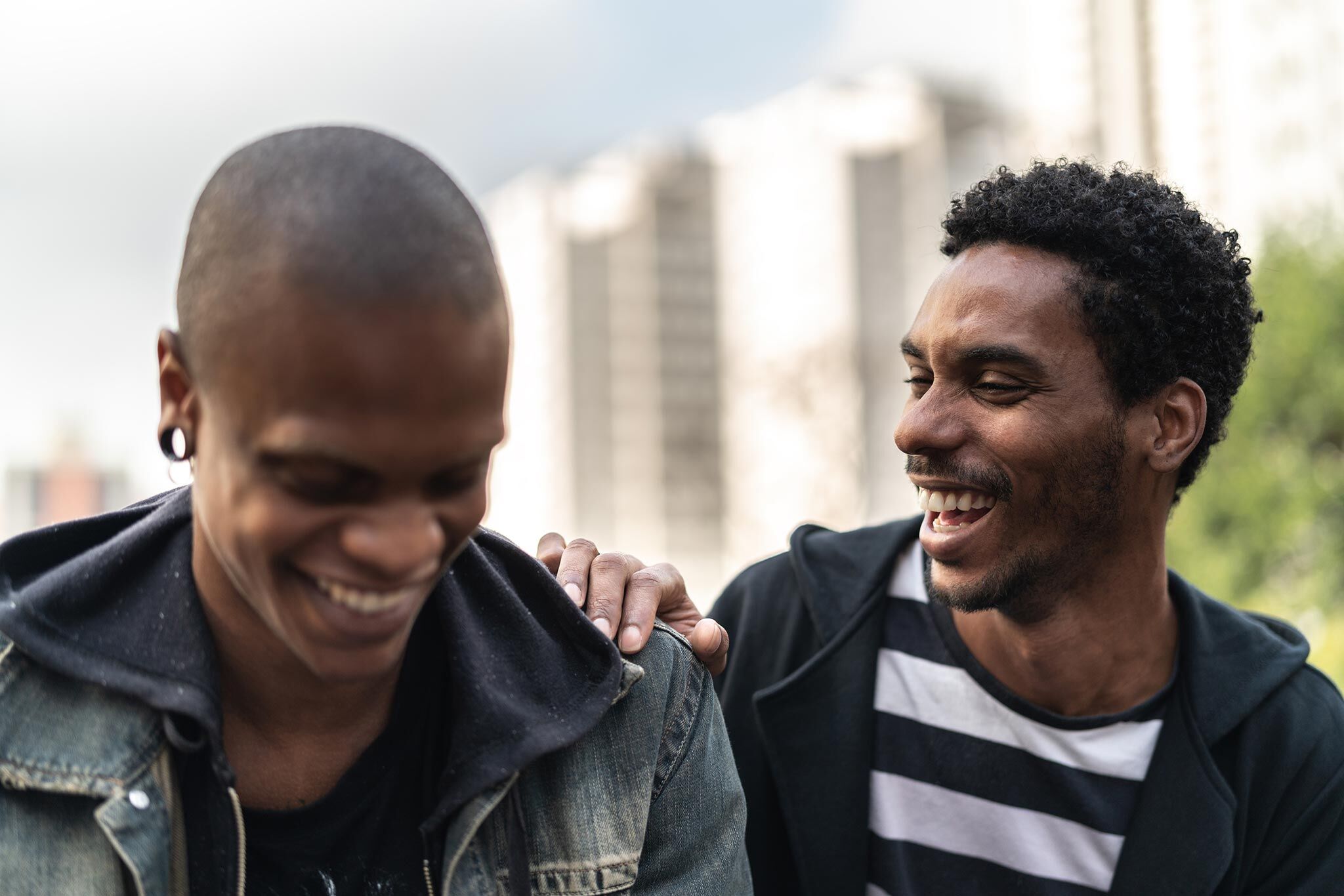 inset-photo-6 Close-up photo of two young men outdoors in an urban location laughing while one places his hand on the other's shoulder.